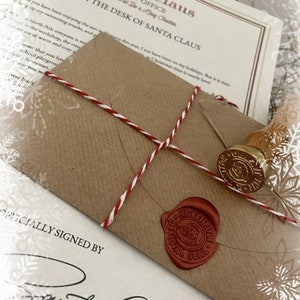 May include: A Christmas-themed image featuring a brown envelope sealed with red wax and a gold stamp. The envelope is tied with red and white twine and rests on a letter from Santa Claus. The letterhead reads "Santa Claus Post Office".