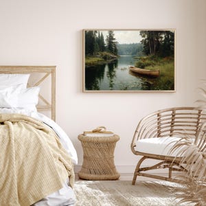 Peut inclure: Une impression encadr&eacute;e d'un paysage paisible avec un bateau en bois sur un lac. L'&oelig;uvre pr&eacute;sente des arbres verts luxuriants, une eau calme et un bateau clair. L'impression est affich&eacute;e au-dessus d'un lit et d'une table d'appoint tress&eacute;e.