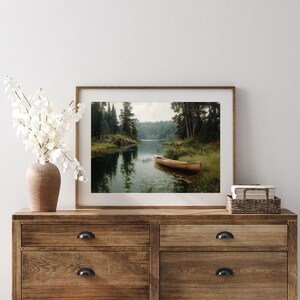 Peut inclure: Une impression encadr&eacute;e d'un paysage paisible avec un bateau en bois sur un lac. L'&oelig;uvre d'art repr&eacute;sente une &eacute;tendue d'eau calme entour&eacute;e d'arbres verts luxuriants et d'une rive lointaine. Le bateau est pr&egrave;s du bord de l'eau, cr&eacute;ant une atmosph&egrave;re sereine.