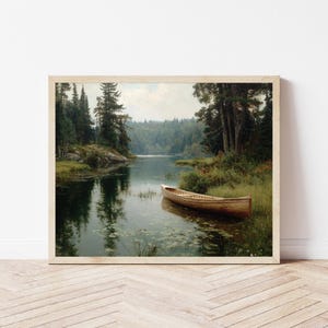 Peut inclure: Une impression encadr&eacute;e d'un paysage paisible. Un bateau en bois est amarr&eacute; pr&egrave;s du rivage, entour&eacute; d'une v&eacute;g&eacute;tation luxuriante et de grands arbres. L'eau refl&egrave;te les arbres et le ciel, cr&eacute;ant une atmosph&egrave;re sereine.