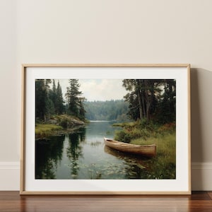 Peut inclure: Une impression encadr&eacute;e d'un paysage lacustre serein. Un bateau en bois est amarr&eacute; pr&egrave;s du rivage, entour&eacute; d'herbe verte et d'arbres. L'&oelig;uvre est encadr&eacute;e dans un cadre en bois clair, ajoutant une touche de charme rustique.