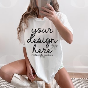 May include: A white oversized t-shirt with the text "your design here" and the words "real people mockups no ai" printed on the front. The model is wearing a beige baseball cap and white cowboy boots.