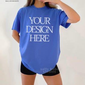 May include: A blue t-shirt with the text "YOUR DESIGN HERE" in white. The shirt is a solid colour and appears to be a mock-up for a design. The model is wearing black shorts.