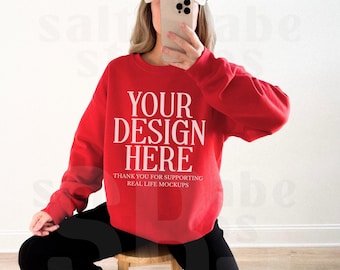 May include: A bright red crewneck sweatshirt featuring the white text "YOUR DESIGN HERE" and "THANK YOU FOR SUPPORTING REAL LIFE MOCKUPS" printed on the chest. The sweatshirt has long sleeves and a ribbed collar, cuffs, and hemline.
