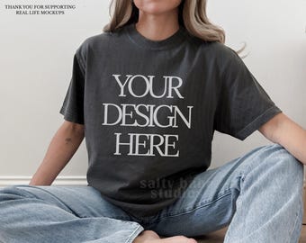 May include: A charcoal gray short-sleeve crew neck t-shirt featuring the white text YOUR DESIGN HERE printed in a serif font on the chest. The shirt is paired with light blue denim jeans, creating a casual and neutral appearance.