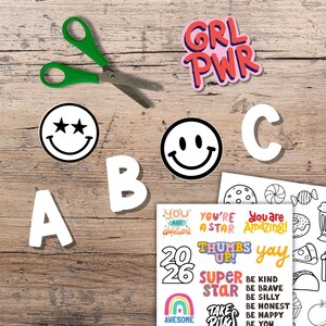 Kids Vision Board 2026 printable cutouts and affirmations shown on wooden table with scissors letters smiley faces and positive quotes like You Are Amazing and Girl Power. Fun DIY goal setting craft and New Year activity for children to color cut and create their own inspiring kids vision board.