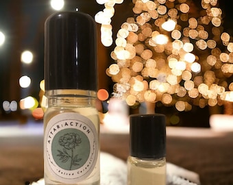 May include: Two glass bottles with black caps and labels. The larger bottle has a label that says "Attar: Action Salted Caramel". The bottles are sitting on a white surface with a blurry background of a Christmas tree with lights.