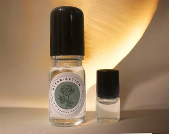 May include: Two glass bottles with black roll-on tops. The larger bottle has a white label with the text "ATTAR: ACTION" and a green floral design.