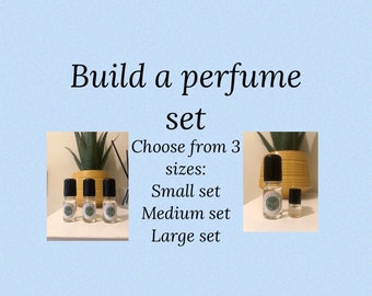 May include: Three small glass bottles with black caps and labels. The bottles are arranged in a row on a wooden surface. The text "Build a perfume set" is written above the bottles. The text "Choose from 3 sizes: Small set, Medium set, Large set" is written below the bottles.
