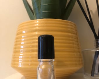 May include: A clear glass roller bottle with a black lid. The bottle is sitting on a white surface.