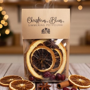 May include: A clear bag of simmering potpourri with dried orange slices, star anise, cinnamon sticks, and cranberries. The bag has a brown paper top with the text "Christmas Blues" and "Simmering Potpourri". Steam rises from the bag.