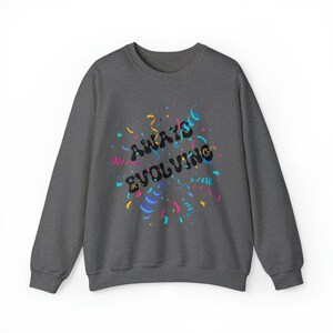 Puede incluir: Una sudadera gris oscuro con el texto "Always Evolving" en letras negras rodeada de confeti de colores.