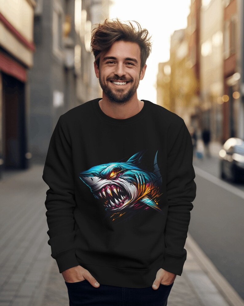 May include: A black sweatshirt with a graphic print of a blue and yellow shark with sharp teeth. The shark is facing the viewer with its mouth open.