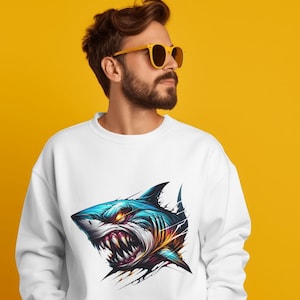 May include: A white sweatshirt with a graphic print of a blue and yellow shark with sharp teeth and angry eyes. The shark is depicted as if it is breaking through the fabric of the shirt.