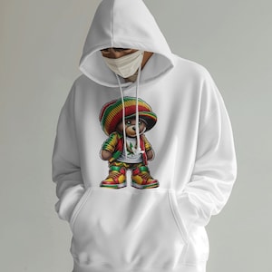 Puede incluir: Sudadera con capucha blanca con un estampado gr&aacute;fico de un oso de dibujos animados que lleva un gorro rojo, amarillo y verde, una chaqueta roja y pantalones amarillos. El oso sostiene una hoja verde de marihuana.