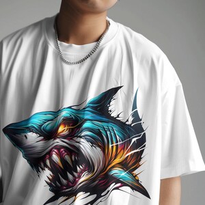 May include: White t-shirt with a graphic print of a blue and white shark with yellow and red accents.