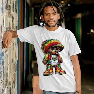 Puede incluir: Una camiseta blanca con una ilustraci&oacute;n de dibujos animados de un oso con un gorro rojo, amarillo y verde, una chaqueta verde y una cadena de oro. El oso sostiene una hoja de marihuana en su mano.