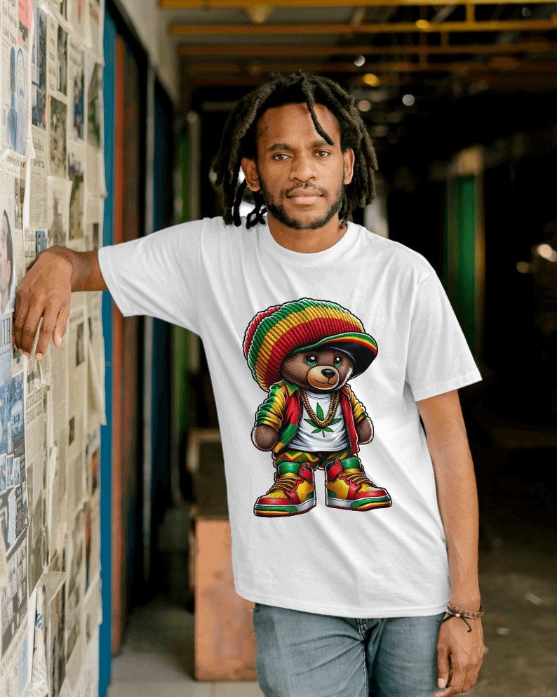 Puede incluir: Una camiseta blanca con una ilustraci&oacute;n de dibujos animados de un oso con un gorro rojo, amarillo y verde, una chaqueta verde y una cadena de oro. El oso sostiene una hoja de marihuana en su mano.