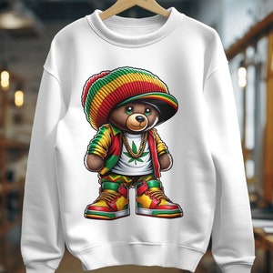 Puede incluir: Sudadera blanca con un gr&aacute;fico de un osito de peluche que lleva una boina roja, amarilla y verde, una camisa verde y amarilla, una chaqueta roja y pantalones verdes, amarillos y rojos. El oso lleva una cadena de oro con un colgante de hoja de marihuana verde y zapatillas rojas, amarillas y verdes.