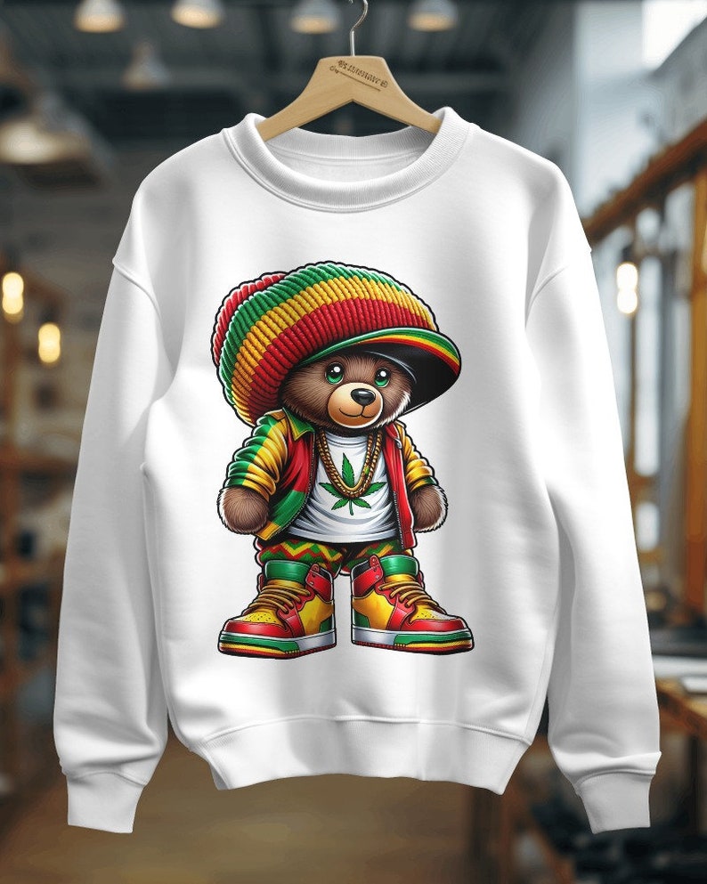 Puede incluir: Sudadera blanca con un gr&aacute;fico de un osito de peluche que lleva una boina roja, amarilla y verde, una camisa verde y amarilla, una chaqueta roja y pantalones verdes, amarillos y rojos. El oso lleva una cadena de oro con un colgante de hoja de marihuana verde y zapatillas rojas, amarillas y verdes.