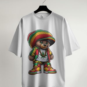 Puede incluir: Camiseta blanca con un gr&aacute;fico de un oso de peluche de dibujos animados que lleva un sombrero rojo, amarillo y verde, una cadena de oro y un dise&ntilde;o de hoja verde. El oso lleva ropa roja, amarilla y verde y zapatillas rojas y amarillas.