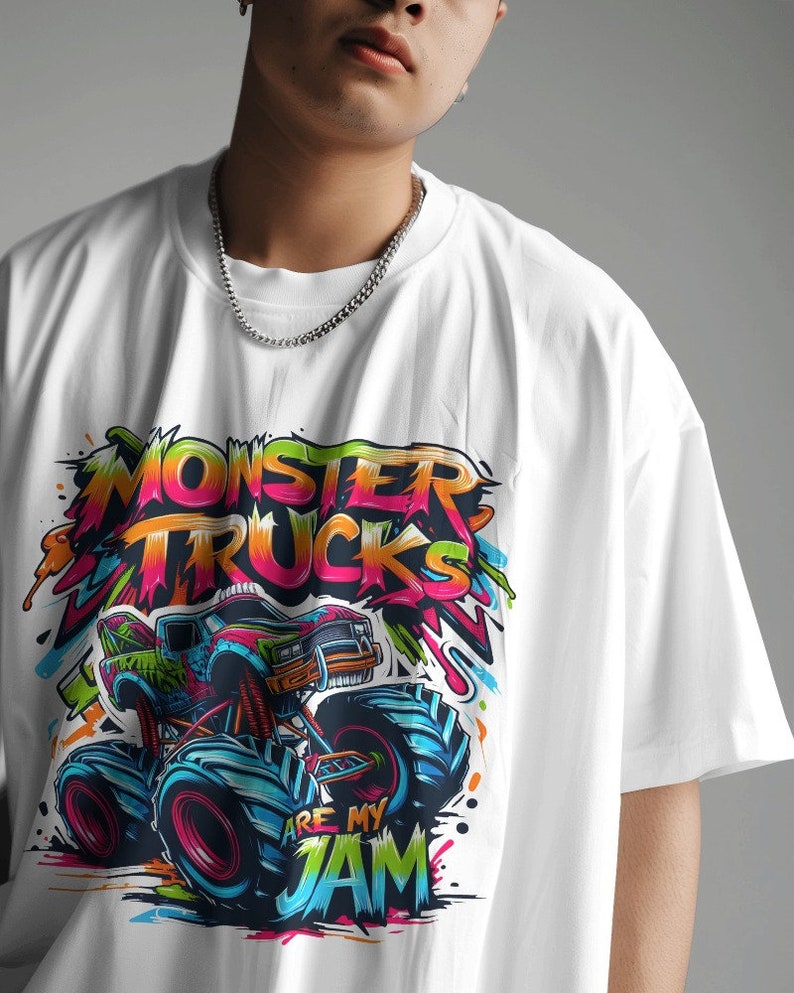 May include: White t-shirt with a colorful graphic of a monster truck. The graphic includes the text "Monster Trucks Are My Jam".