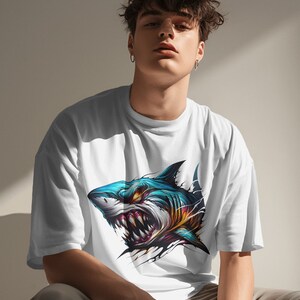 May include: A white t-shirt with a graphic print of a blue and yellow shark with sharp teeth. The shark is shown with its mouth open and its eyes are glowing red.