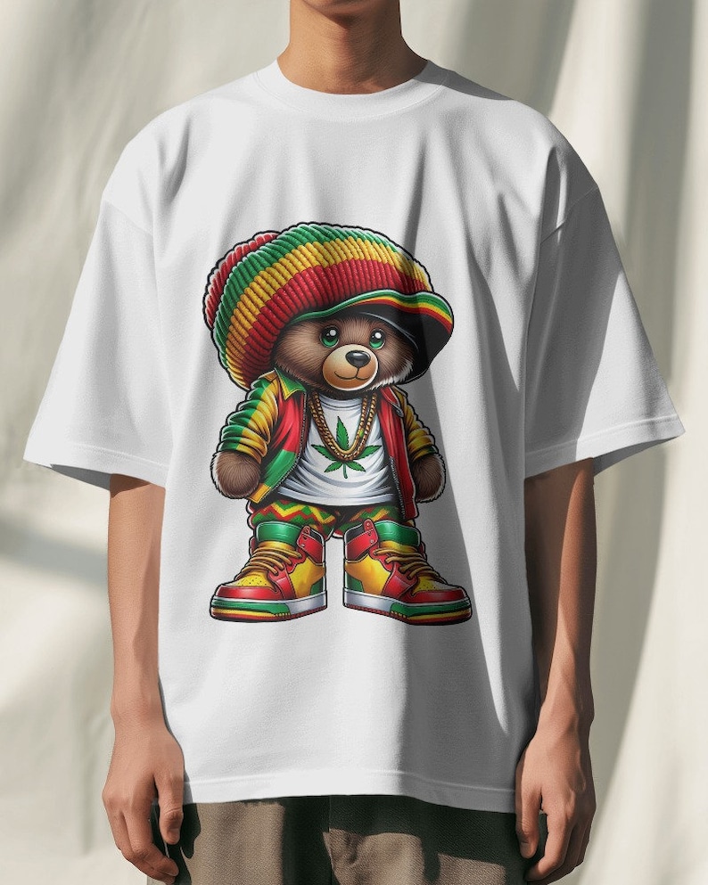 Puede incluir: Camiseta blanca con una ilustraci&oacute;n de dibujos animados de un oso de peluche con un sombrero rojo, amarillo y verde, una chaqueta verde y amarilla y pantalones verde y amarillo. El oso lleva una cadena de oro con un colgante de hoja de marihuana verde. El oso lleva zapatillas rojas, amarillas y verdes.