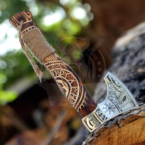 May include: A hand-crafted axe with a wooden handle and a steel head. The handle is decorated with intricate carvings and the head features a Viking design. The axe is a decorative piece and is not intended for use.