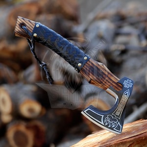 May include: A black and silver axe with a wooden handle wrapped in black leather. The axe has a Celtic knot design and a bear paw print on the blade. The handle is decorated with a wood grain pattern.