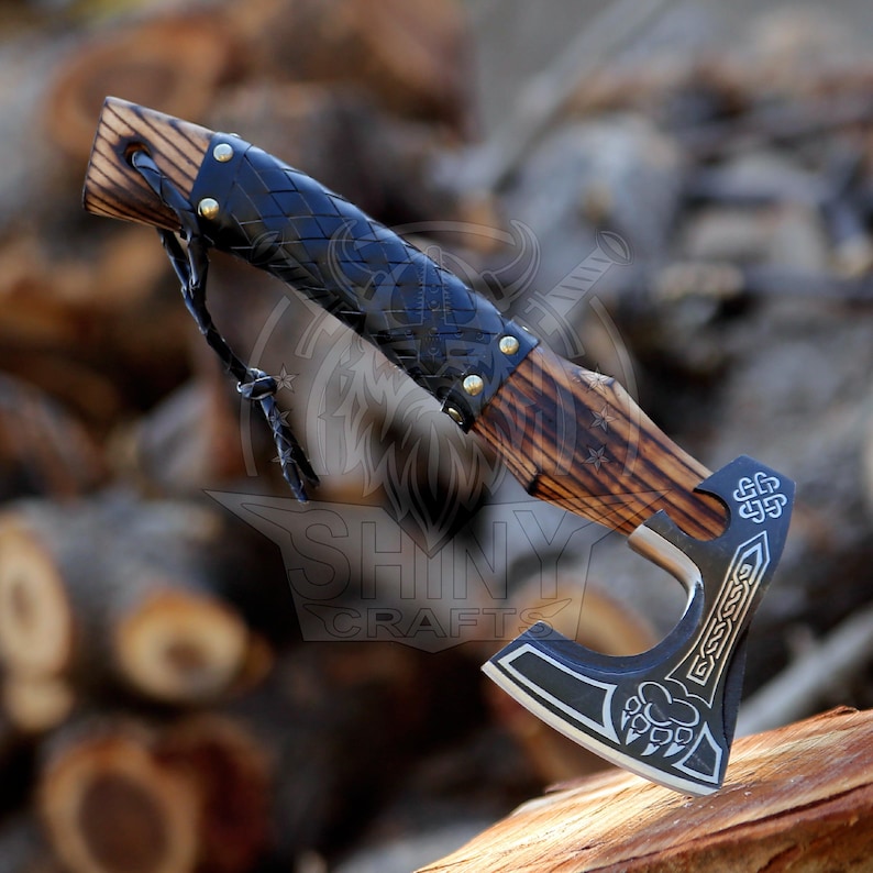 May include: A black and silver axe with a wooden handle wrapped in black leather. The axe has a Celtic knot design and a bear paw print on the blade. The handle is decorated with a wood grain pattern.