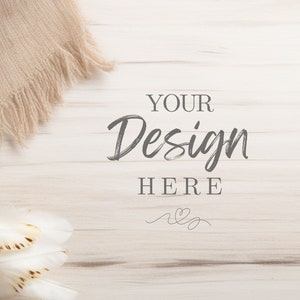 May include: A neutral-toned mockup featuring a beige fringed scarf and white feathers on a light wood-grain surface. The text "YOUR Design HERE" is displayed in a handwritten style, with a small heart design below.