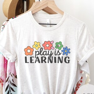 Soft t-shirt that says "Play is Learning" and has cute retro flowers on it for preschool teacher, play therapist, or speech therapist. Gift for teachers or therapists.