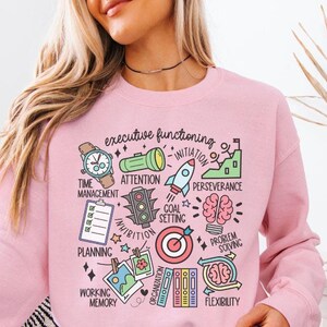 May include: Light pink sweatshirt with a graphic print of various icons representing executive functioning skills. The icons include a clock, a traffic light, a rocket ship, a target, a brain, and more. The text "executive functioning" is printed at the top of the graphic.