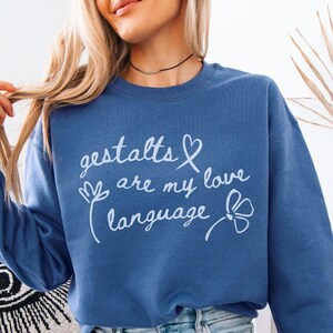 May include: Indigo blue sweatshirt with the text "gestalts are my love language" in white script. The design includes a heart and floral accents. The bottom of the sweatshirt has the text "INDIGO BLUE".
