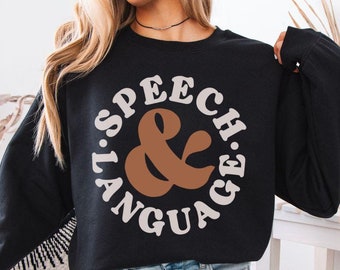 Puede incluir: Sudadera negra con un gráfico circular blanco que dice "Speech & Language" en una fuente retro. La ampersand es marrón.