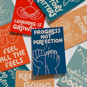 May include: A collection of colorful cards with motivational phrases and illustrations. The cards feature text like "Progress Not Perfection," "Feel All The Feels," and "Learning is Growing." The designs include hand-drawn images and a variety of bright colors.