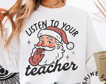 Könnte beinhalten: Weißes Sweatshirt mit einem Weihnachtsmann-Motiv und dem Text "Listen to your teacher". Die Santa-Illustration hat einen roten Hut und Handschuhe, mit einem weißen Bart und Schnurrbart. Das Sweatshirt hat lange Ärmel.