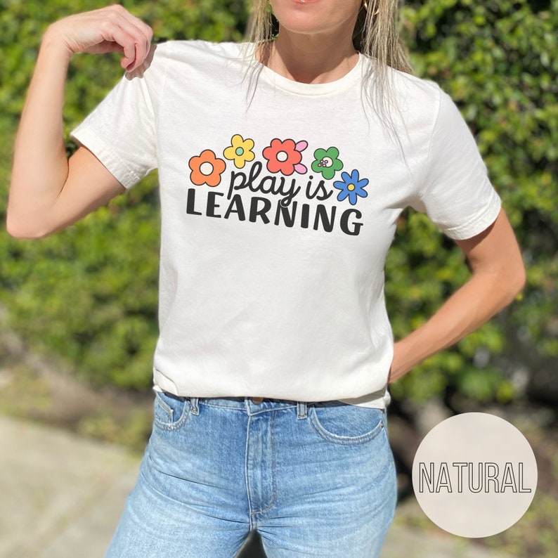 Woman wearing t-shirt that says "Play is Learning" and has cute retro flowers on it for preschool teacher, play therapist, or speech therapist. Gift for teachers or therapists.