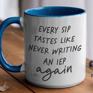 May include: White ceramic mug with a blue interior and handle. The mug features the text "EVERY SIP TASTES LIKE NEVER WRITING AN IEP again" in black script. The mug is on a wooden surface.