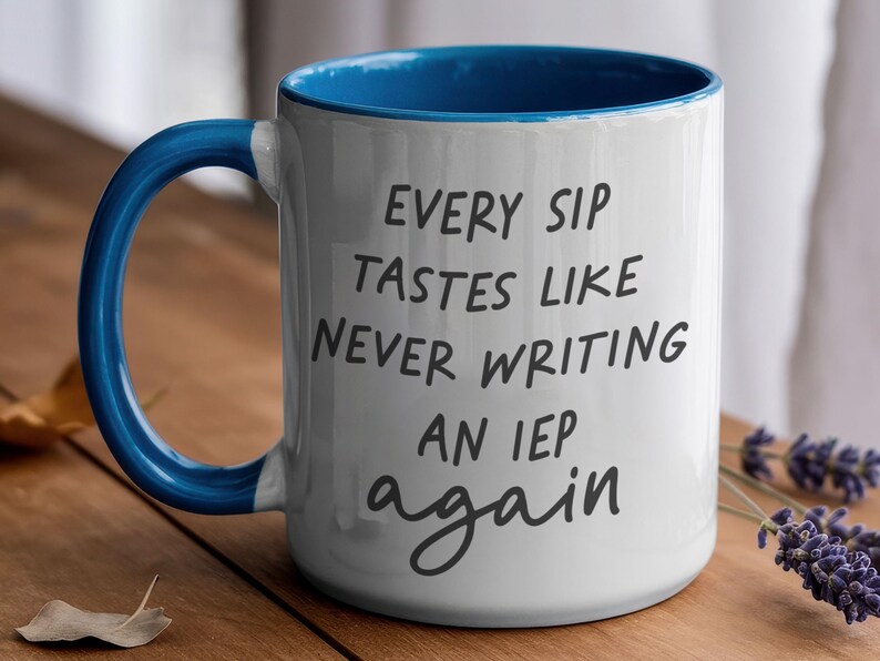 May include: White ceramic mug with a blue interior and handle. The mug features the text "EVERY SIP TASTES LIKE NEVER WRITING AN IEP again" in black script. The mug is on a wooden surface.