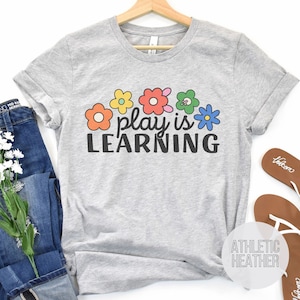 Soft t-shirt that says "Play is Learning" and has cute retro flowers on it for preschool teacher, play therapist, or speech therapist. Gift for teachers or therapists.