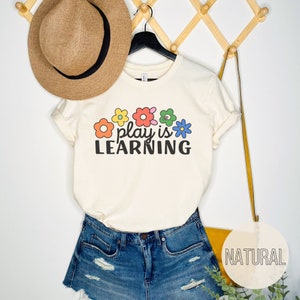 Soft t-shirt that says "Play is Learning" and has cute retro flowers on it for preschool teacher, play therapist, or speech therapist. Gift for teachers or therapists.