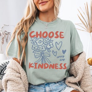 Comfort colors 1717 shirt that says Choose Kindness in large bold hand written font and has doodle images of a bouquet of flowers with a bow and hearts and the words every day written smaller in doodle cursive.