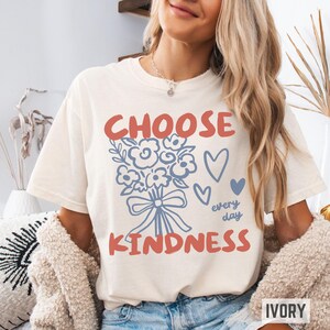 Comfort colors 1717 shirt that says Choose Kindness in large bold hand written font and has doodle images of a bouquet of flowers with a bow and hearts and the words every day written smaller in doodle cursive.
