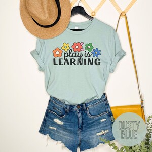 Soft t-shirt that says "Play is Learning" and has cute retro flowers on it for preschool teacher, play therapist, or speech therapist. Gift for teachers or therapists.