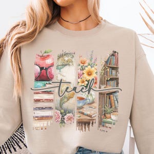 Puede incluir: Sudadera beige con un diseño gráfico que presenta una pila de libros, un globo terráqueo, flores y una taza de té. El gráfico está rodeado por un borde pintado y la palabra "teach" está escrita sobre el diseño.