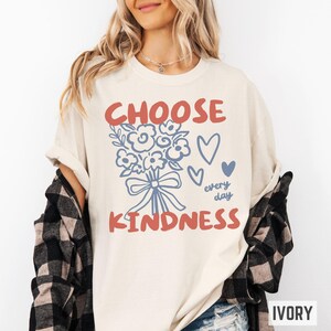 Comfort colors 1717 shirt that says Choose Kindness in large bold hand written font and has doodle images of a bouquet of flowers with a bow and hearts and the words every day written smaller in doodle cursive.