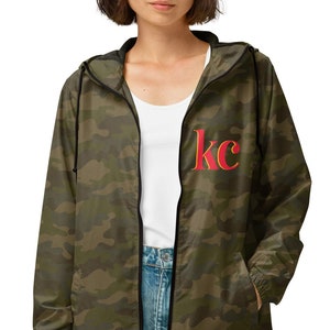 Brunette woman wearing Camo Kansas City unisex lightweight zip up windbreaker with printed KC on left chest pocket.