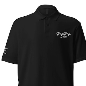 May include: Black polo shirt with short sleeves and a white embroidered logo that says "Pop Pop est 2024".